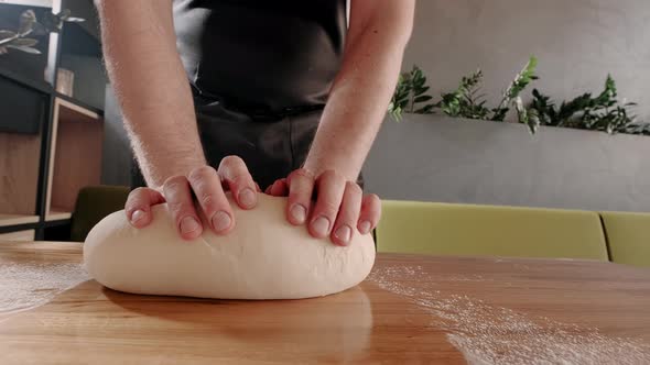 Man Baker Kneads Dough for Baking and Bread on Wooden Table