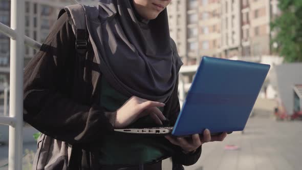 Unrecognizable Young Confident Woman in Hijab Typing on Laptop Keyboard in City. Portrait of Busy