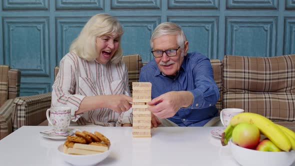 Retired Senior Couple Spending Time Together Playing Game with Wooden Blocks on Table in Living Room