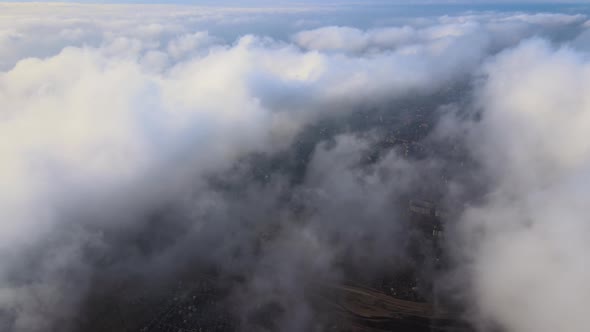 Aerial View From High Altitude of Distant City Covered with Puffy Cumulus Clouds Flying By Before