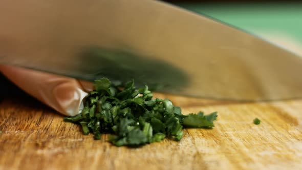 cutting parsley with knife above a wooden cutting board, side view