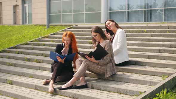 Young Girls Businesswomen Sit on the Stairs and Browse the Contents of Documents in a Black Folder