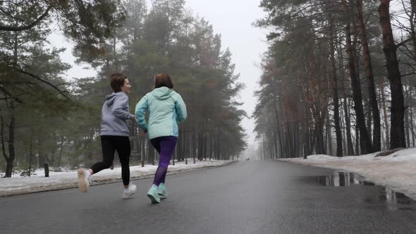 Happy Senior and Young Attractive Women Running in The Snowy Park in Winter Talking and Smiling