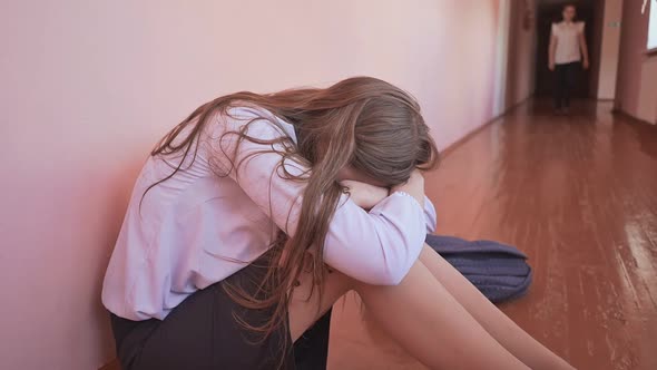 A Female Student is Crying on the Floor of a Corridor at School