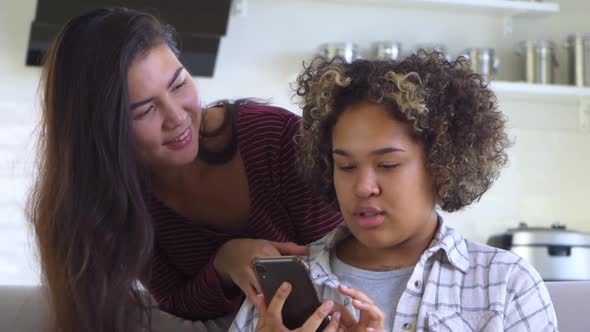 A Girl Hugs Her Friend From Behind Who is Holding a Smartphone