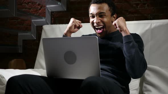 Happy African Man Celebrating Success of Work on Laptop