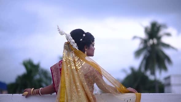 Sad and upset Indian Bengali bride looking at dark cloudy sky on monsoon evening