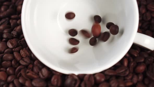 Roasted dark coffee beans fall into a white ceramic cup 