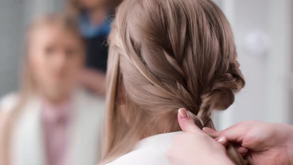 Female Hairdresser Plaiting Braid on Long Blonde Hair Back View Closeup