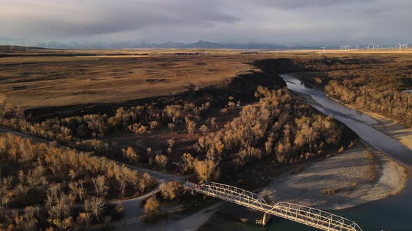 Red pick-up truck traveling through vast countryside landscape and crossing an old steel bridge over