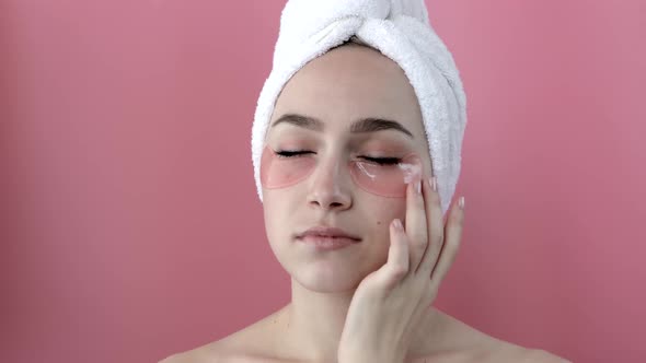 Plesant nude girl applying collagen eye masks on face in front of a mirror.