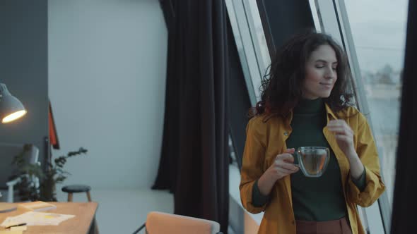 Businesswoman Holding Tea and Looking through Window in Office