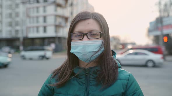 A Young Girl in Glasses and a Medical Mask Stands on the Street