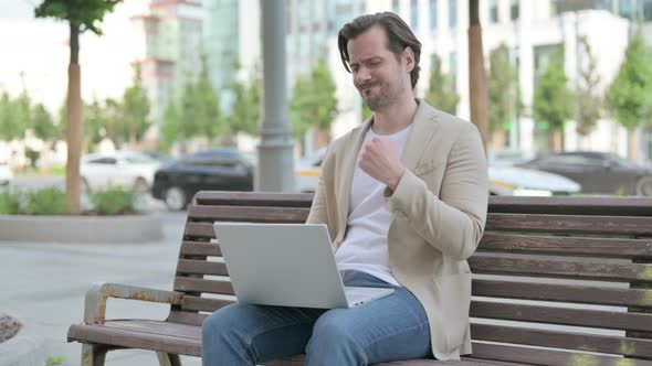 Young Man with Wrist Pain Using Laptop While Sitting on Bench