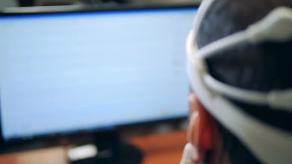 Man Works with Computer, Wearing Sensoring Headset, Back View