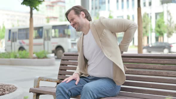 Young Man Having Back Pain While Sitting on Bench