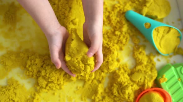 Close up of kids hands playing with yellow magic sand, top view