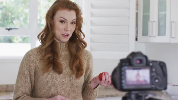 Woman talking while holding tomatoes and recording it with digital camera in the kitchen