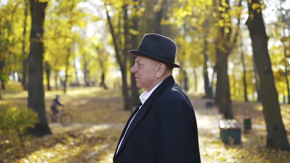 Mature Man Crossing Hands and Turns at Camera with Smile in Autumn Park