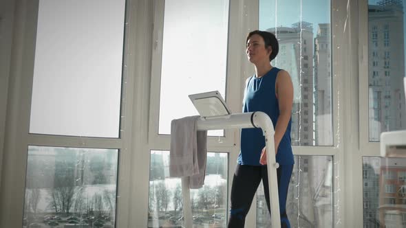 Young smiling woman is exercising on treadmill at home