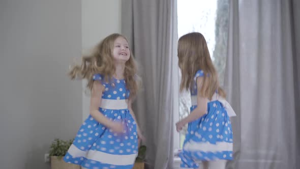 Joyful Pretty Caucasian Girls in Elegant Blue Dotted Dresses Jumping and Spinning at Home. Portrait