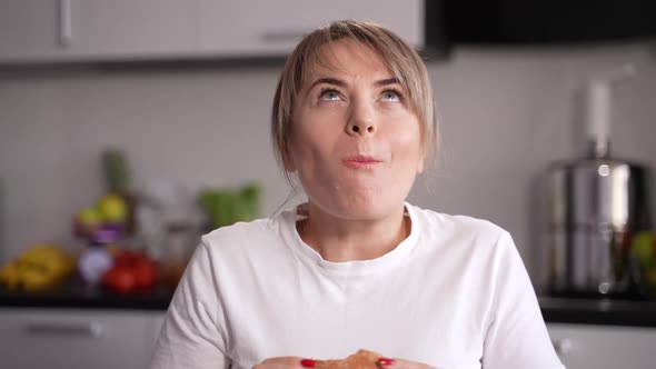 Happy Woman Eating Burger with Pleasure in Kitchen
