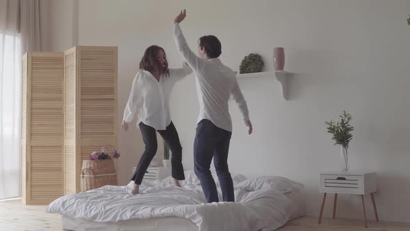 Happy Couple Dancing on the Bed in the Room at Home or Hotel Together. Young Woman Jumping and