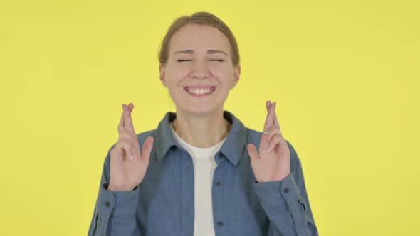 Young Woman Praying with Fingers Crossed on Yellow Background