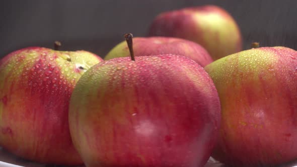 Fresh sweet red apples are spinning on a plate on a black background.