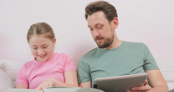 Close Up of Father Holding a Tablet and Laughing Teen Daughter Sitting on the Sofa and Looking at