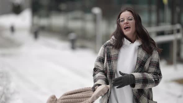 Playful Young Woman is Walking in City at Winter Day and Playing with Hat Singing and Smiling