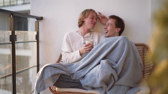 Handsome gay couple talking on the balcony under a blanket
