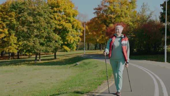 Aged Woman Doing Nordic Walking in Sunny Fall Park By Herself Front View