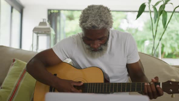 Video of sad african american senior man playing the guitar and using laptop