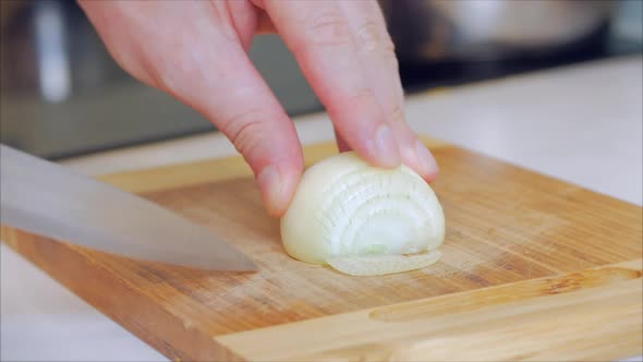 Close-up Woman's Hand Cuts Onion Into Rings on a Split Board at Home in Her Kitchen.