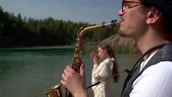 a Saxophonist Plays a Soulful Composition for His Girlfriend in Nature Near a Forest Lake