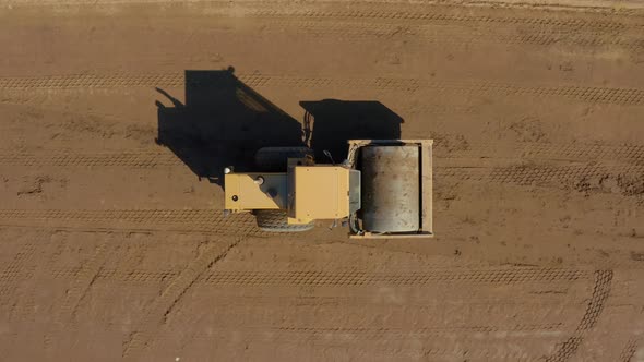 Top down following aerial shot of a Bulldozer Roller compacting dirt on a sunny day