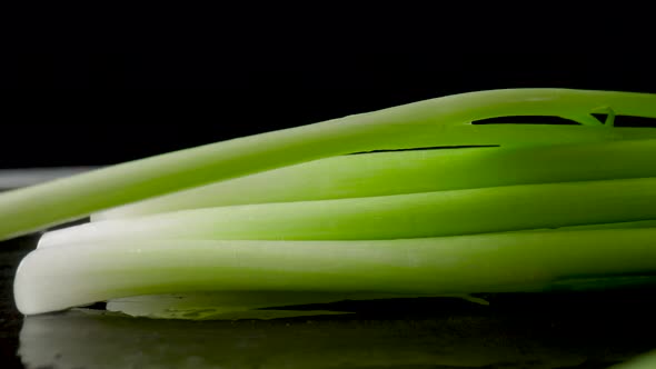 Fresh Green Onion Stalks with Water Drops Falling on the Black Surface of a Wooden Table