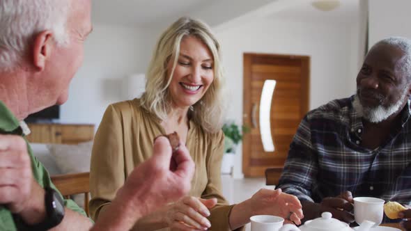 Two diverse senior couples sitting by a table drinking tea together at home