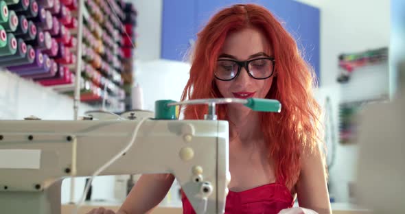 Smiling Female Dressmaker Using Sewing Machine During Sewing Dress in Studio