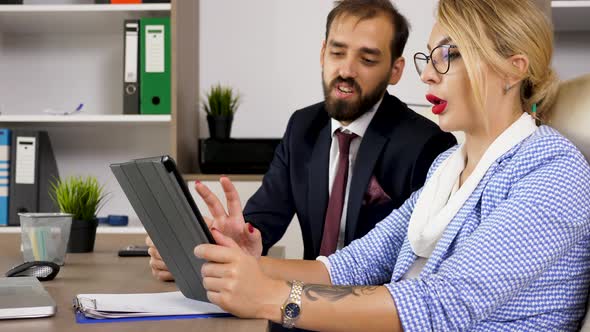 Businesswoman and Businessman at Desk in the Office Looking at Tablet PC