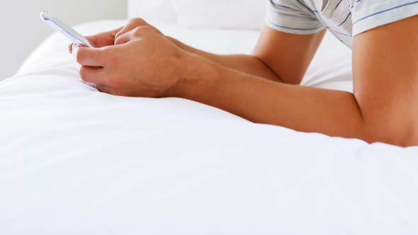 Smiling man using mobile phone on bed in bedroom