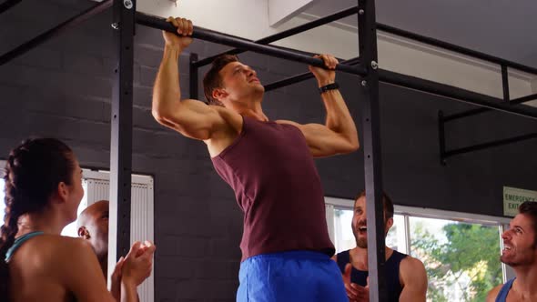 Men performing pull-up exercise while friends applauding him