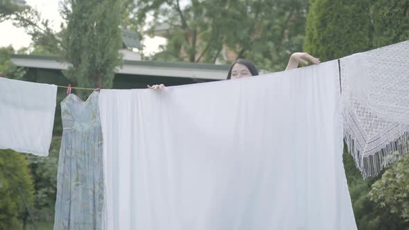 Cute Mature Woman with Long Hair Hanging White Clothes on a Clothesline Looking at Camera Outdoors