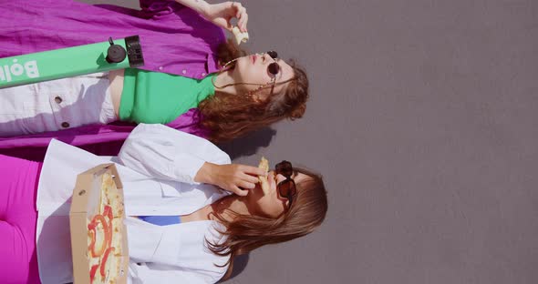 Chernivci, Ukraine - 14.08.2022: two girls appetizingly eat pizza near gray wall