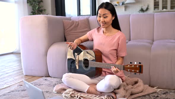 An Attractive Young Asian Woman is Playing Guitar at Home