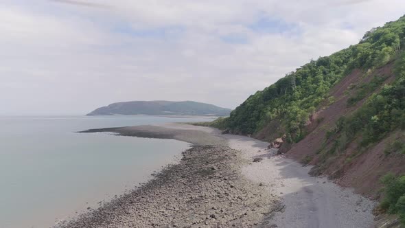 Wide aerial tracking forward with the sea on the left. A head of land in the distance and an amazing