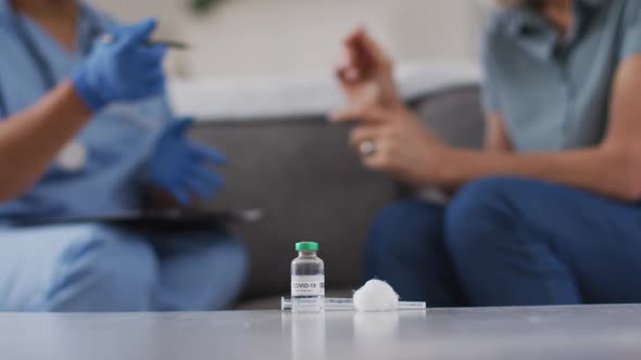 Midsection of african american female doctor talking with female patient at home with vaccination in