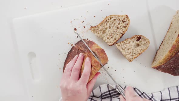 Flat lay. Slicing freshly baked sourdough wheat bread on a white cutting board.