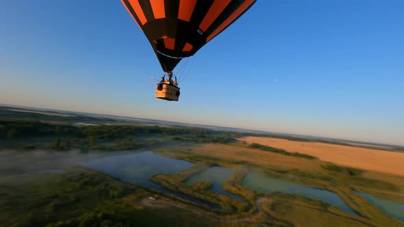 hot air ballon floating above sloping field at beautiful sunrise